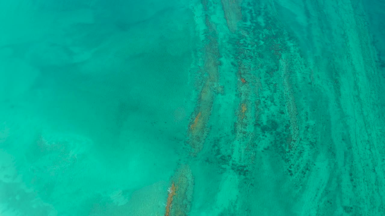 Turquoise Cabo Pulmo water fills the frame as dark reef textures cross pale seabed areas, no visible people.