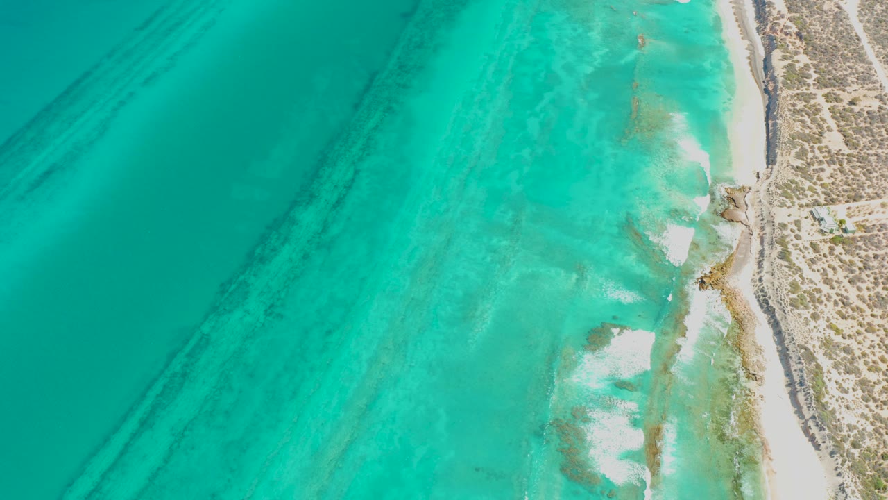 Turquoise coastal water spreads across the left and center while pale surf breaks near the Cabo Pulmo sand and scrub, with no visible people.