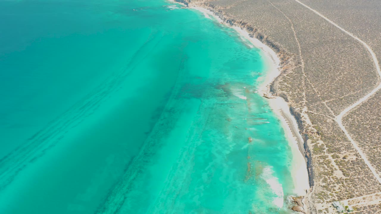 Aerial view of turquoise ocean beside a sandy desert coastline