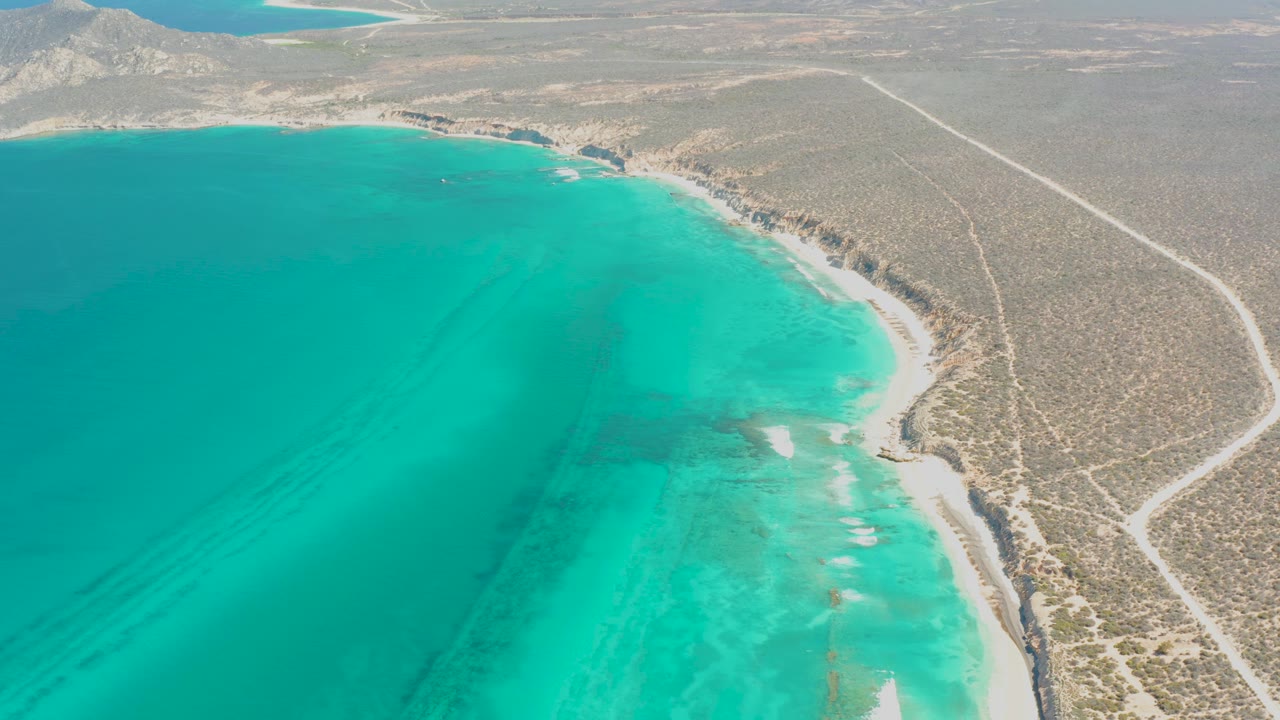 Aerial view of turquoise water beside a dry desert shoreline and dirt road.