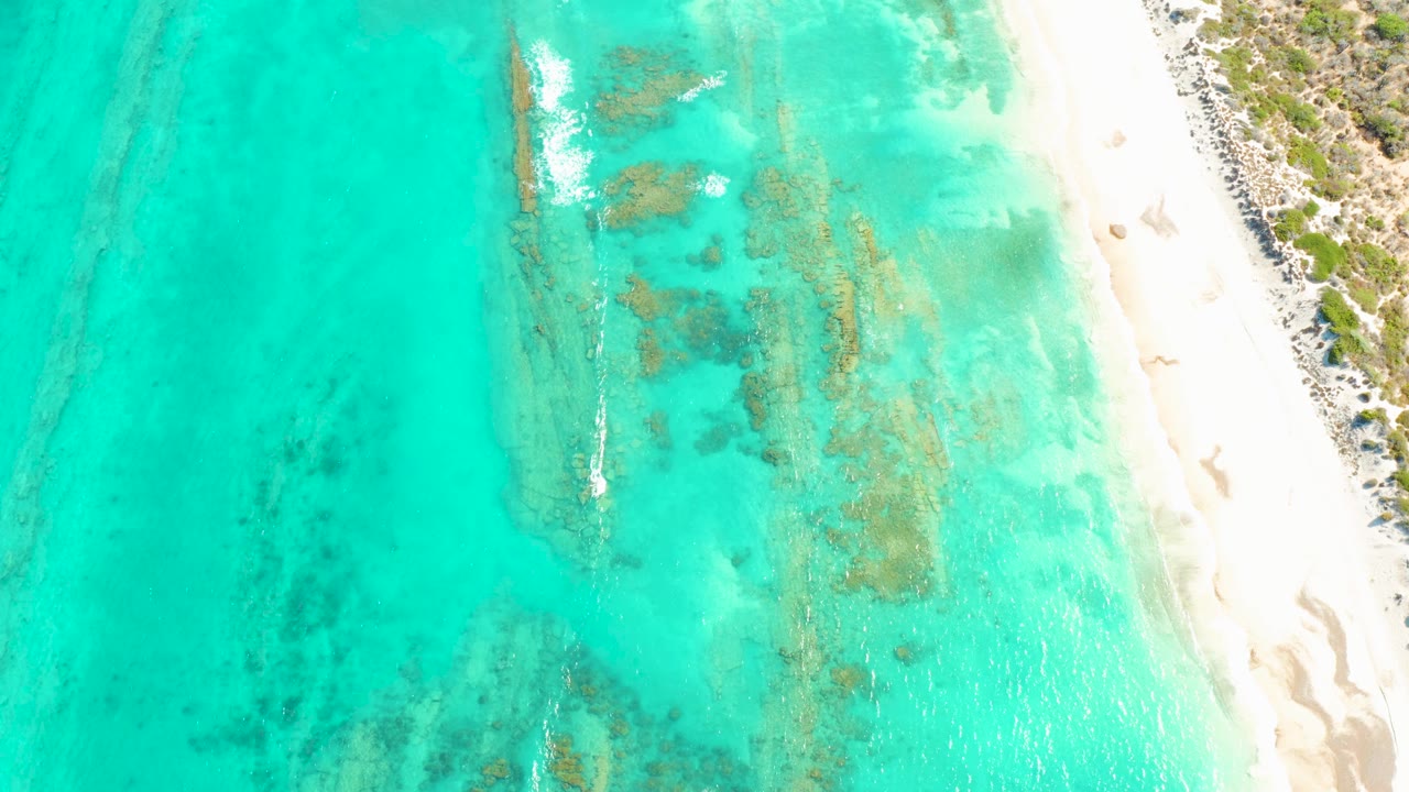 Cabo Pulmo shallows show a long submerged rock formation near center, pale beach along the right side, and no visible people.
