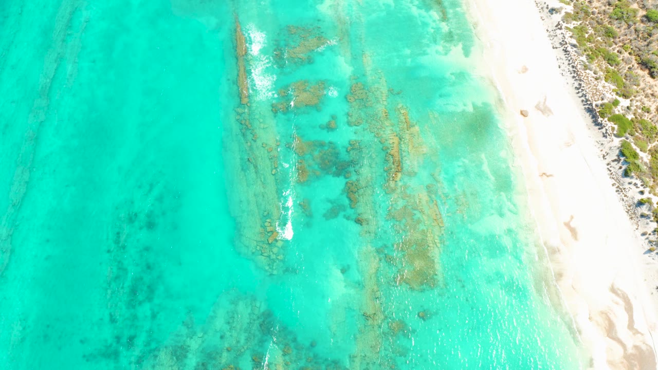 Cabo Pulmo shoreline appears from above with open turquoise water on the left, reef texture through the middle, white beach on the right, and no visible people.