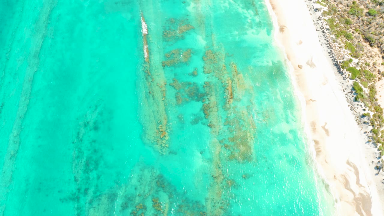 Overhead turquoise water beside a white sand beach with reef patches and a small boat.