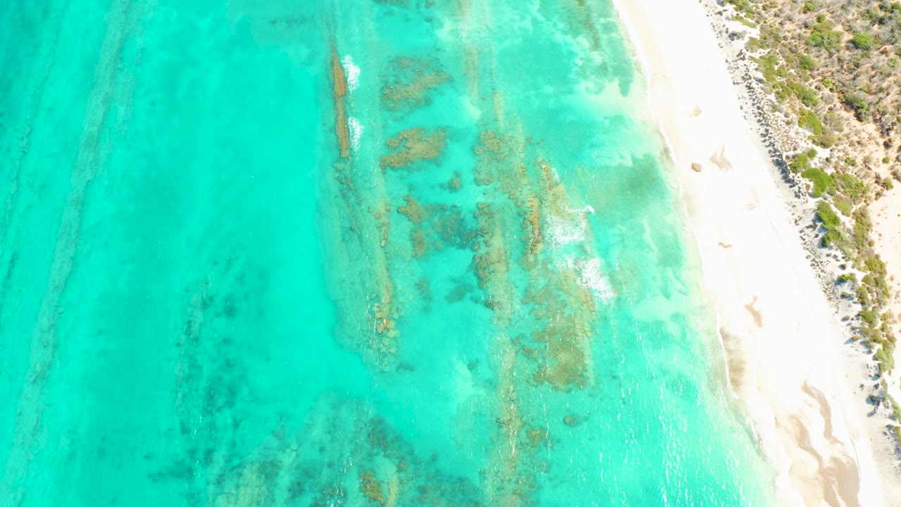 Cabo Pulmo aerial frame with clear turquoise shallows, darker underwater patches near the center, pale sand along the right edge, and no visible people.