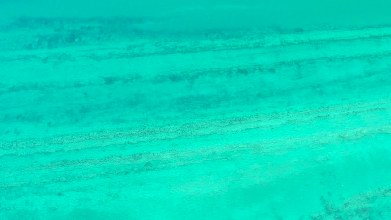 Clear shallow water shows darker horizontal seabed streaks beneath the turquoise surface in Cabo Pulmo, with no visible people.