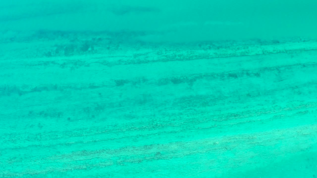 Underwater Cabo Pulmo frame with blue-green water and darker horizontal ridges crossing the sea floor, with no visible people.