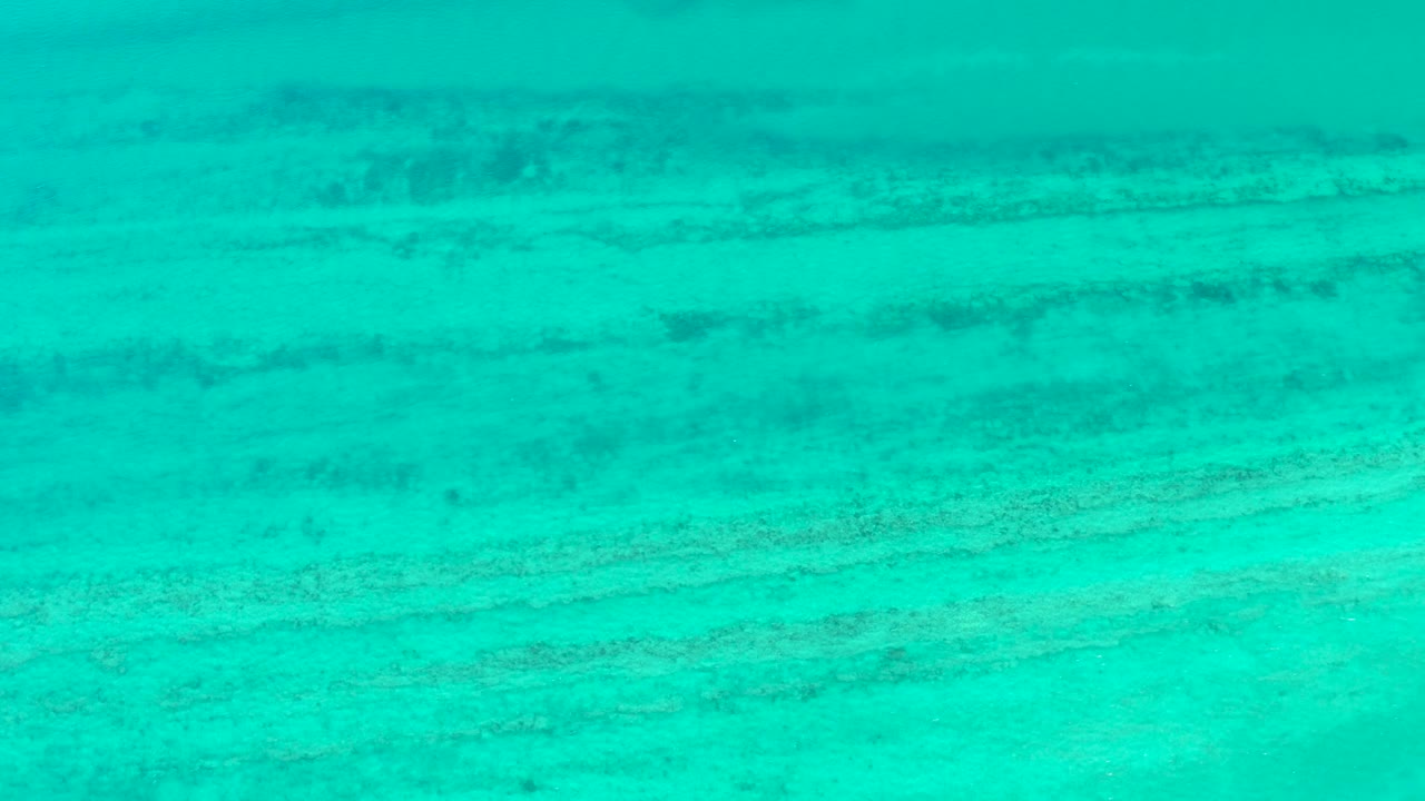 Clear blue-green water with darker seabed streaks
