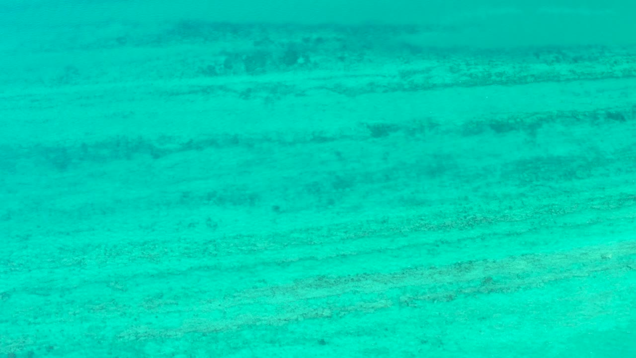 Turquoise water over pale seabed with dark horizontal formations.