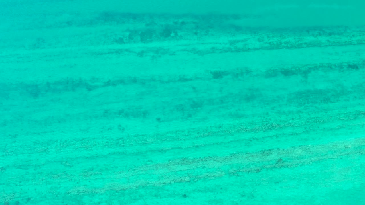 Clear blue-green water in Cabo Pulmo shows darker seabed bands running across the frame, with no visible people.