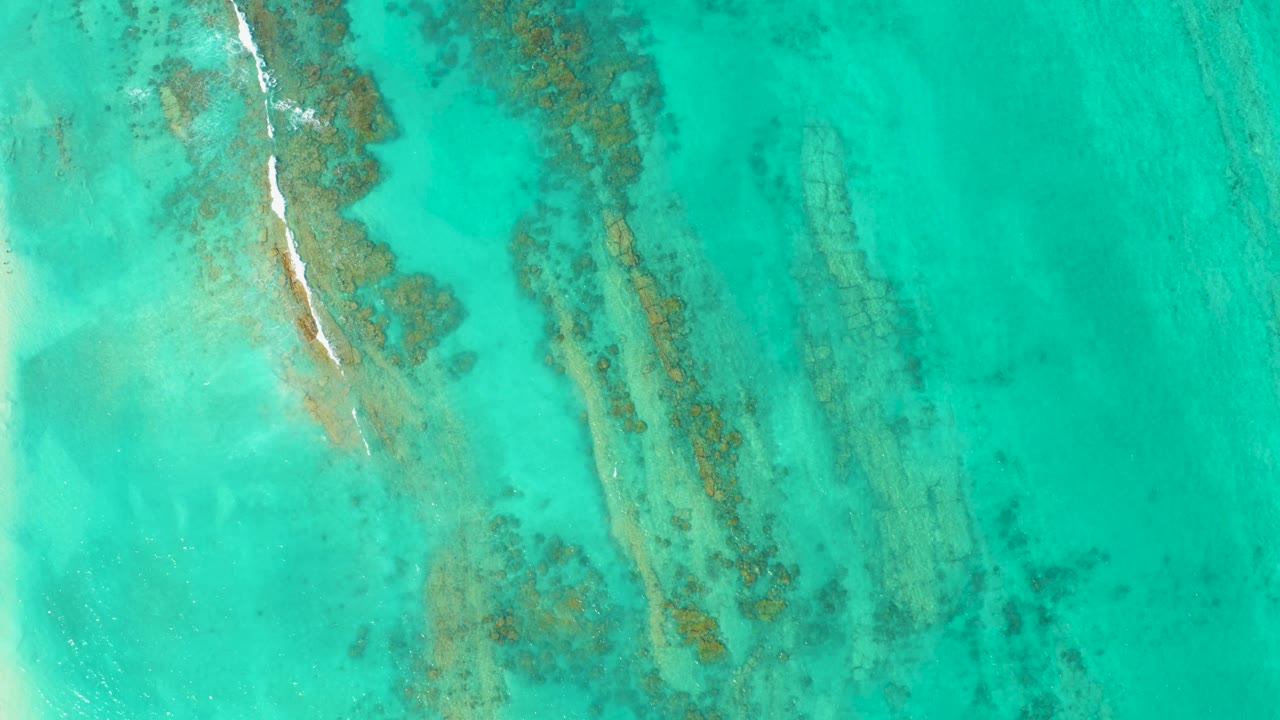 Overhead turquoise water with diagonal reef and white surf line.