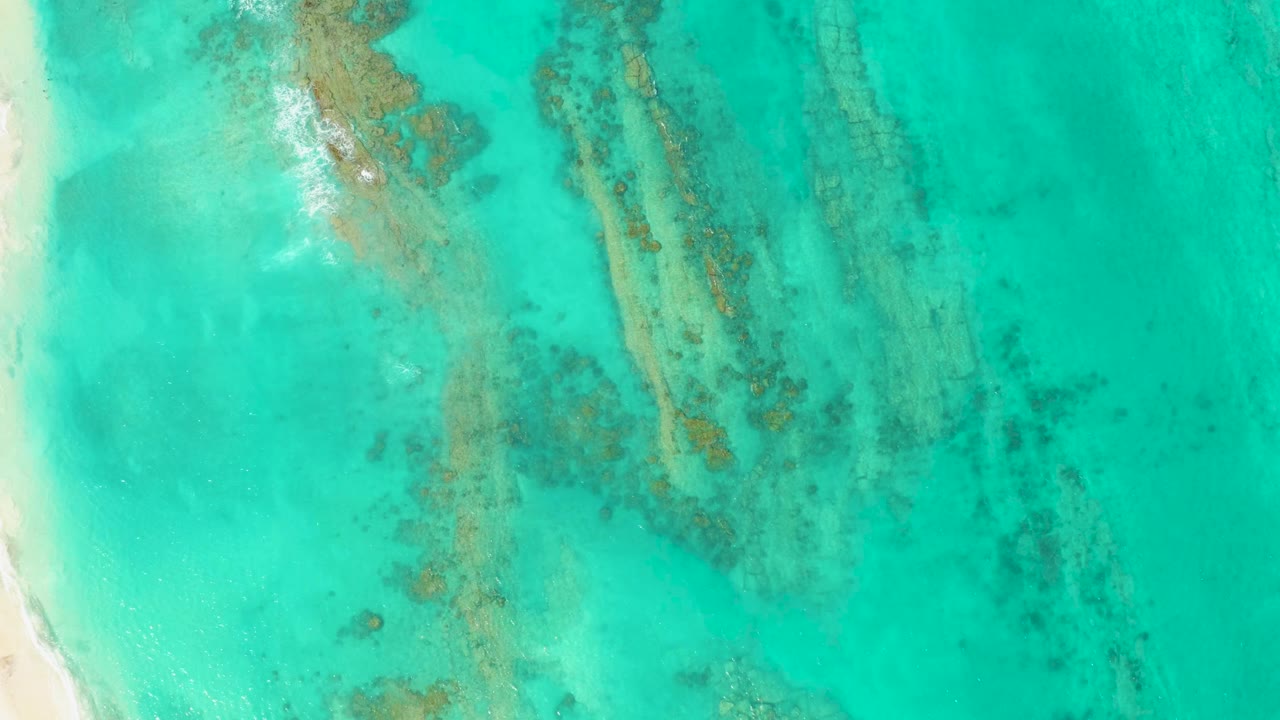 Clear turquoise water over coral bands with sand visible at the left edge.