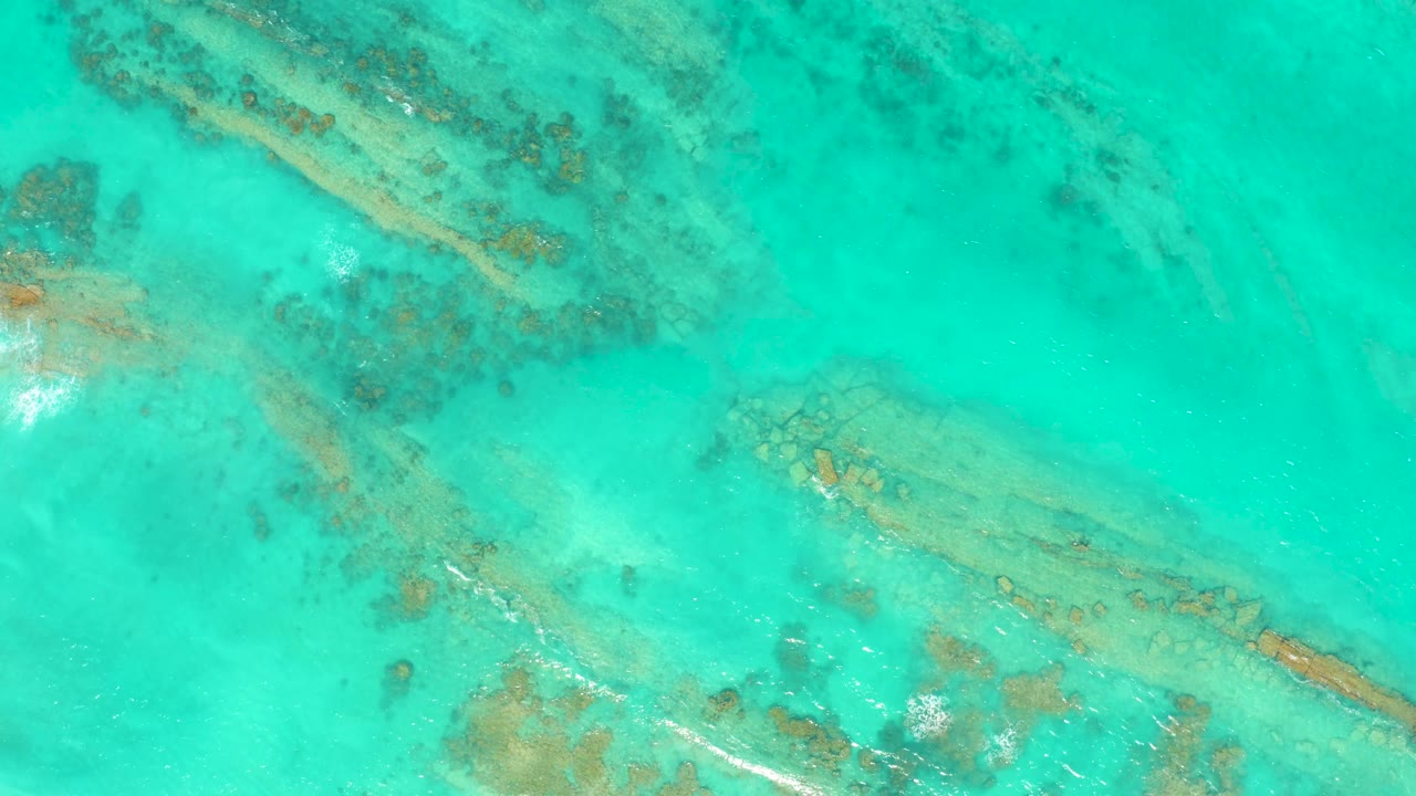 Clear turquoise ocean in Cabo Pulmo shows diagonal reef bands below the surface, with faint white water near the coral and no visible people.