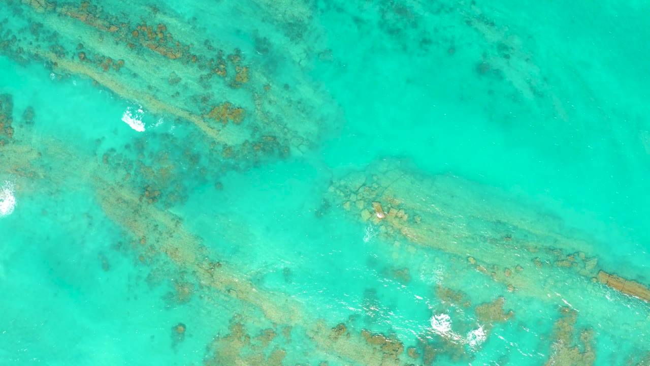 Top-down view of Cabo Pulmo shallows with two visible coral ridges, white water glints along the left and lower areas, and no visible people.