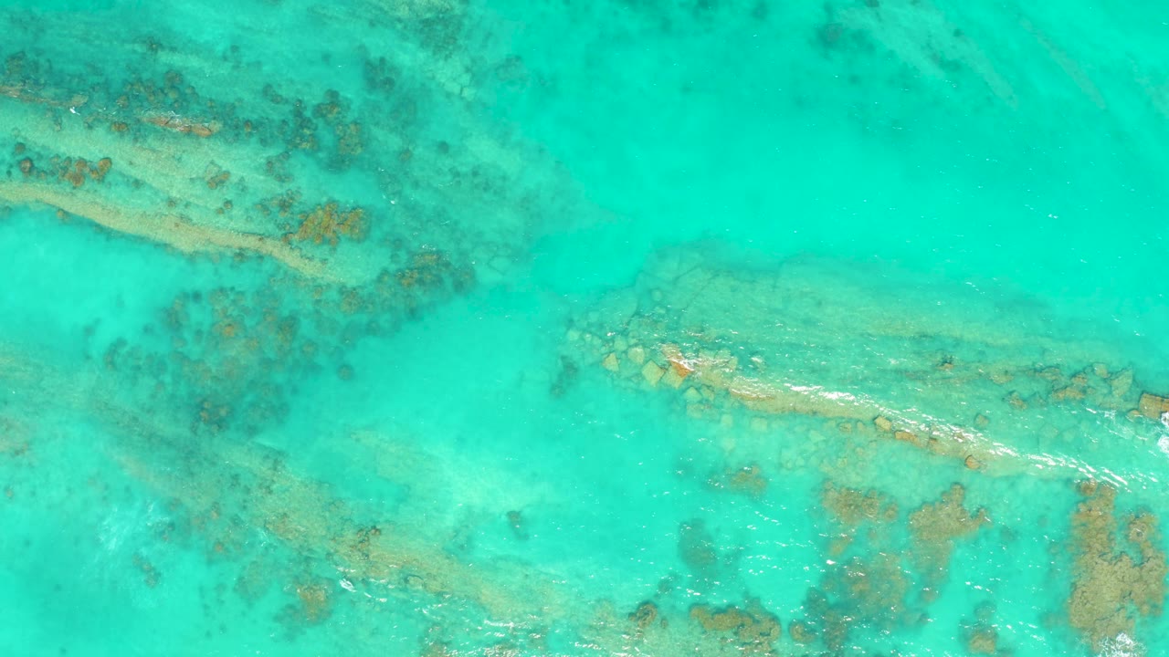 Overhead view of clear turquoise water in Cabo Pulmo with reef patches visible below and no clearly visible swimmer at the opening moment.