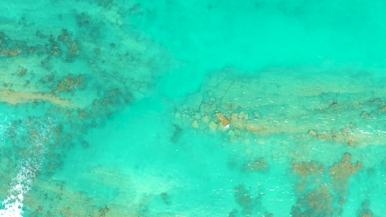 Cabo Pulmo water fills the frame with blue-green color, dark coral patches near the upper left, pale rock below the surface, and no visible people.