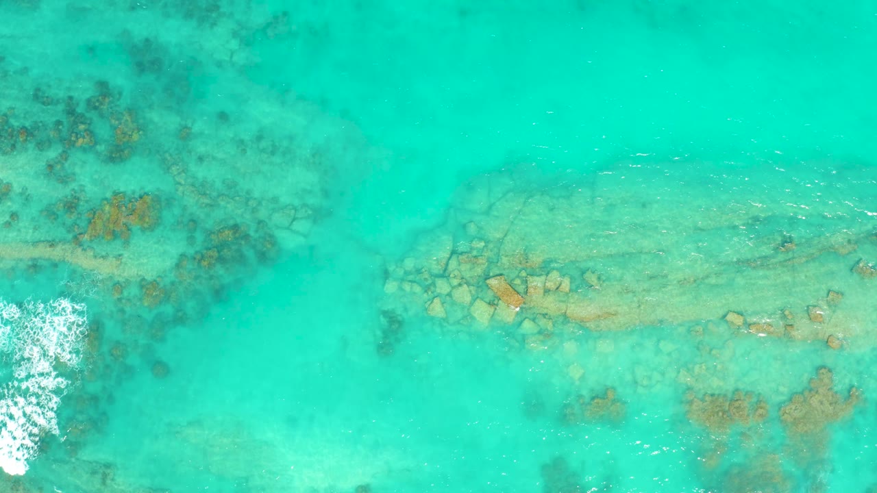 Turquoise ocean shallows with reef below and white surf touching the left border.