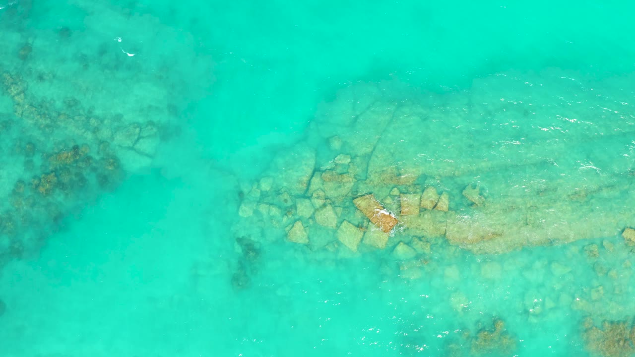 Overhead view of clear turquoise water in Cabo Pulmo, Baja California Sur, with pale rocks below the surface, darker reef patches near the edges, and no visible people.
