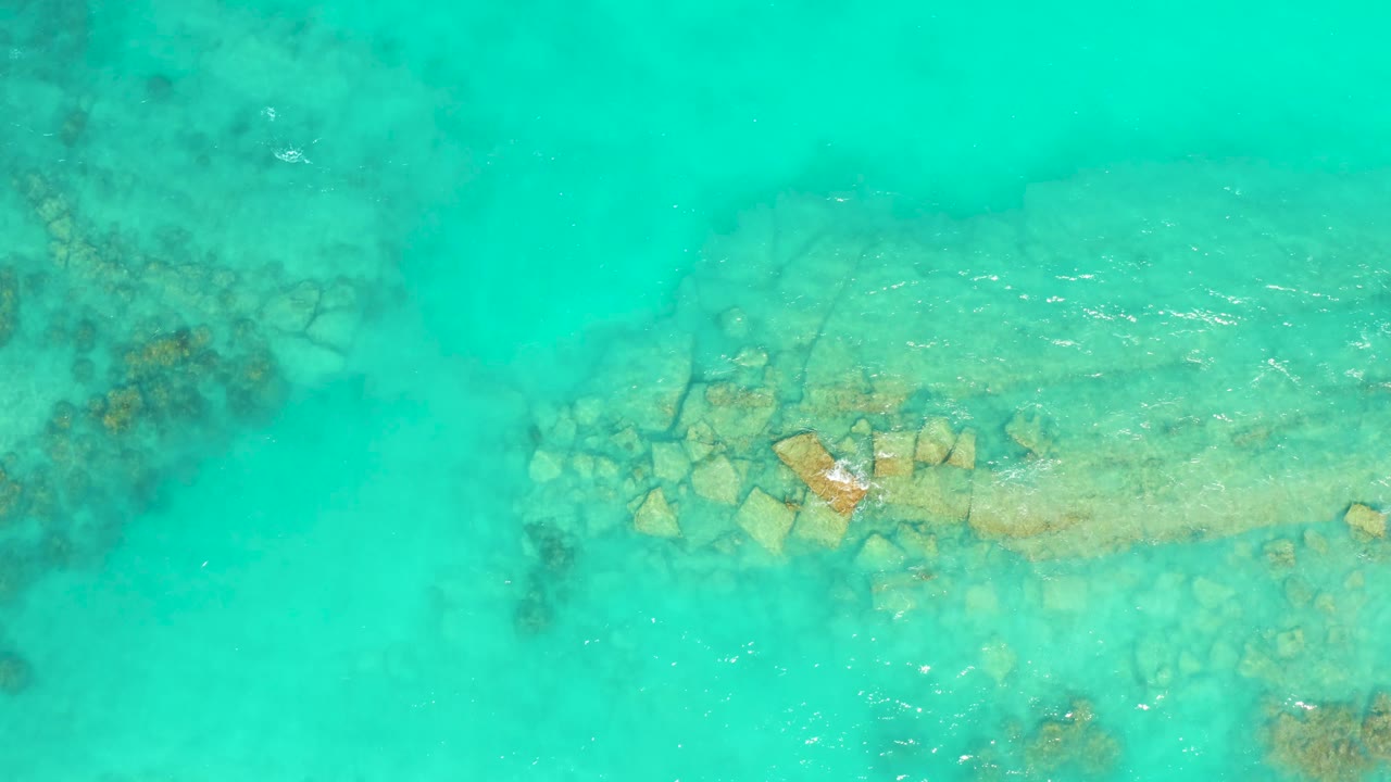 An overhead Cabo Pulmo frame shows bright turquoise water over a pale seabed, with darker reef areas left and right and no visible people.