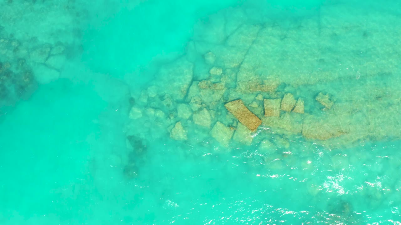 Clear turquoise water in Cabo Pulmo shows tan rock formations below the surface, with brighter ripple highlights along the lower center and no visible people.