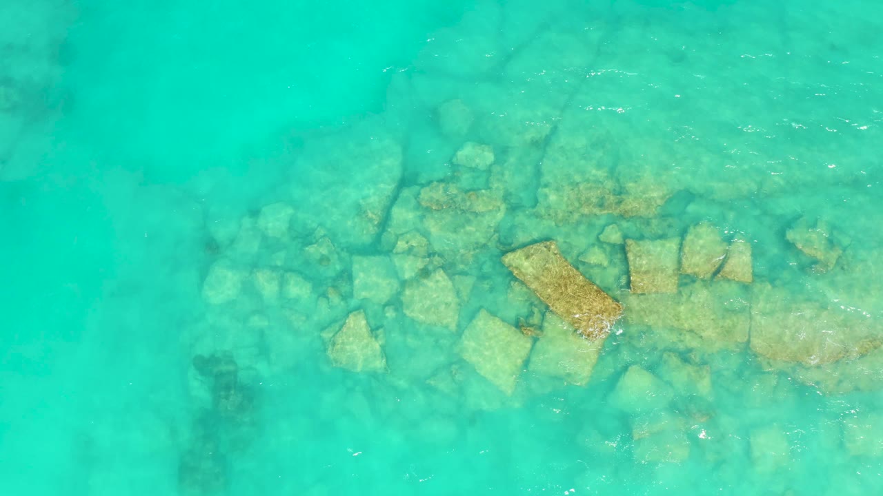 Aerial frame over Cabo Pulmo water shows the same rock cluster under a slightly shifted band of surface shimmer, with no visible people.