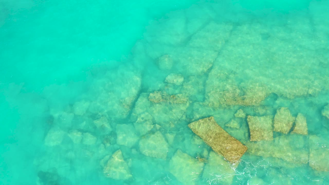 Overhead view of turquoise water in Cabo Pulmo flowing over pale rocks and a larger tan slab, with no visible people.