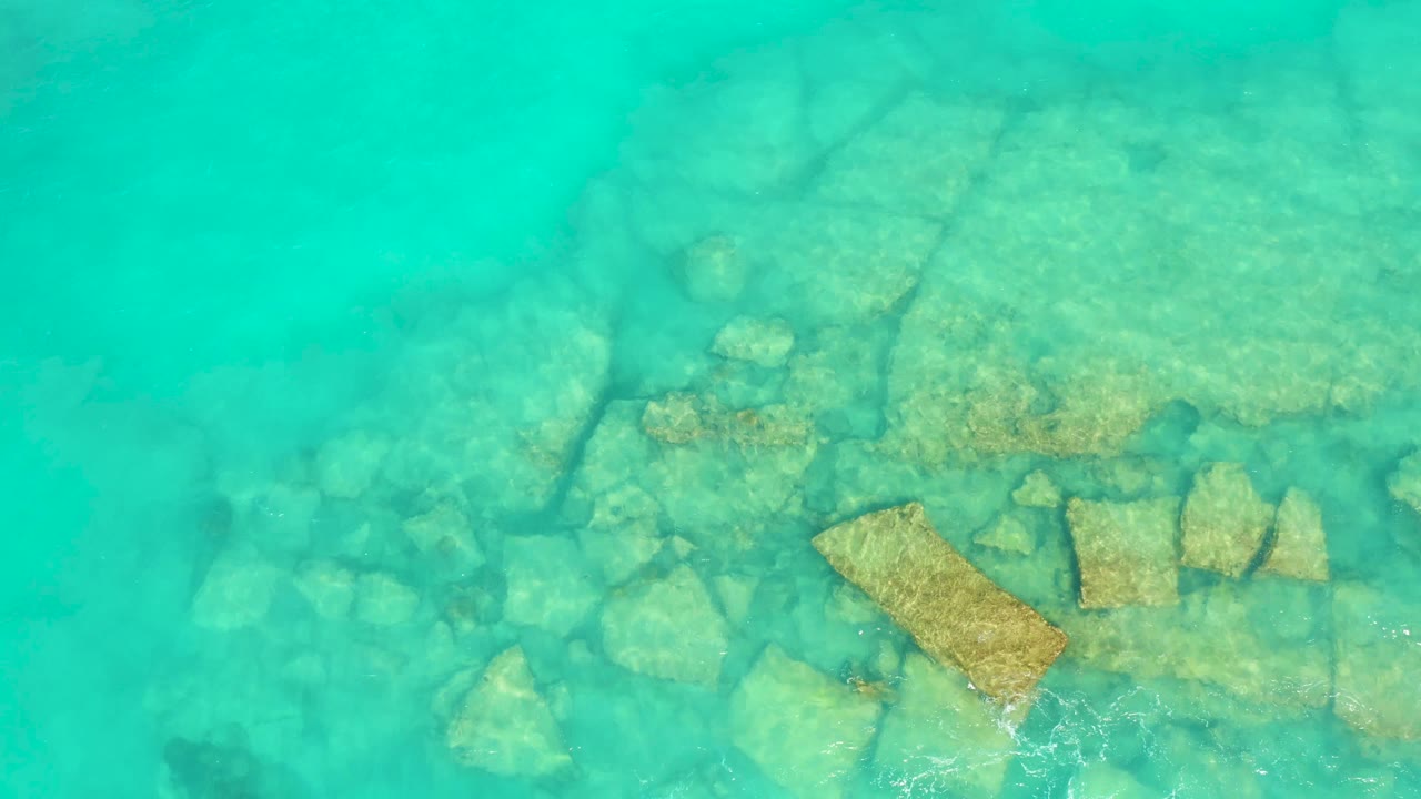 Clear turquoise water in Cabo Pulmo covers clustered seabed rocks, with the tan slab near the lower center and no visible people.
