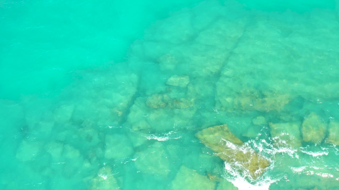 Clear blue-green water showing submerged rocks and white foam over a tan rock slab.