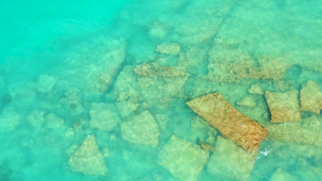 Cabo Pulmo shallow water shows a cluster of submerged rocks and tan rectangular slabs beneath soft surface ripples, with no visible people.