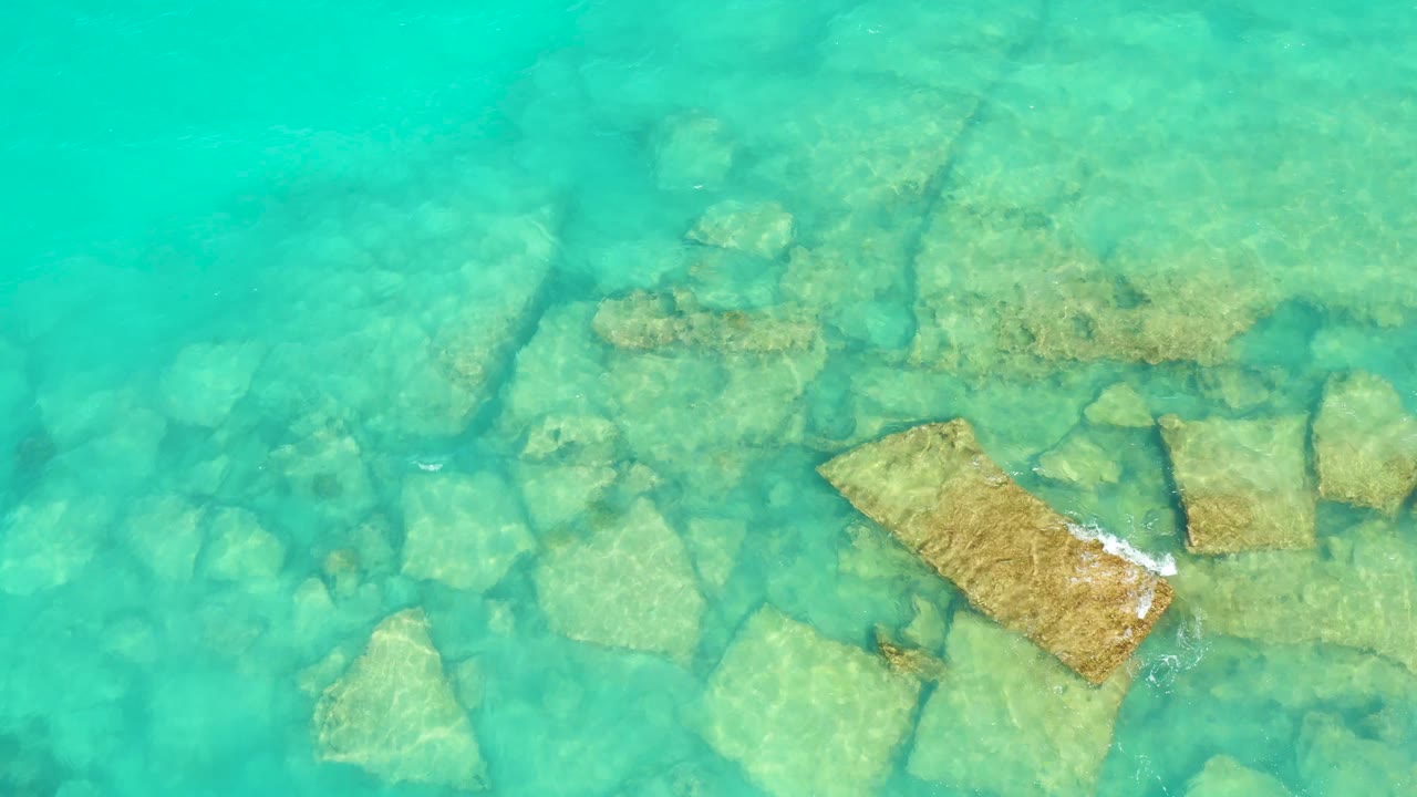 Turquoise water and submerged rocks with white foam crossing a stone block.