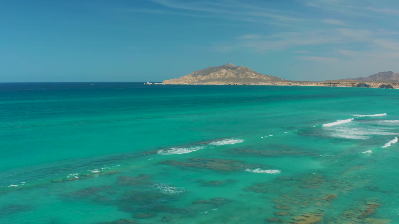 Cabo Pulmo blue-green water fills the frame with visible reef shadows, a thin whitecap pattern across the shallows, distant land at the horizon, and no visible people.