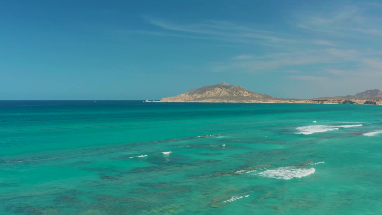 Cabo Pulmo shallow turquoise water stretches toward a low distant landmass, with small white surf lines shifting across the midground and no visible people.