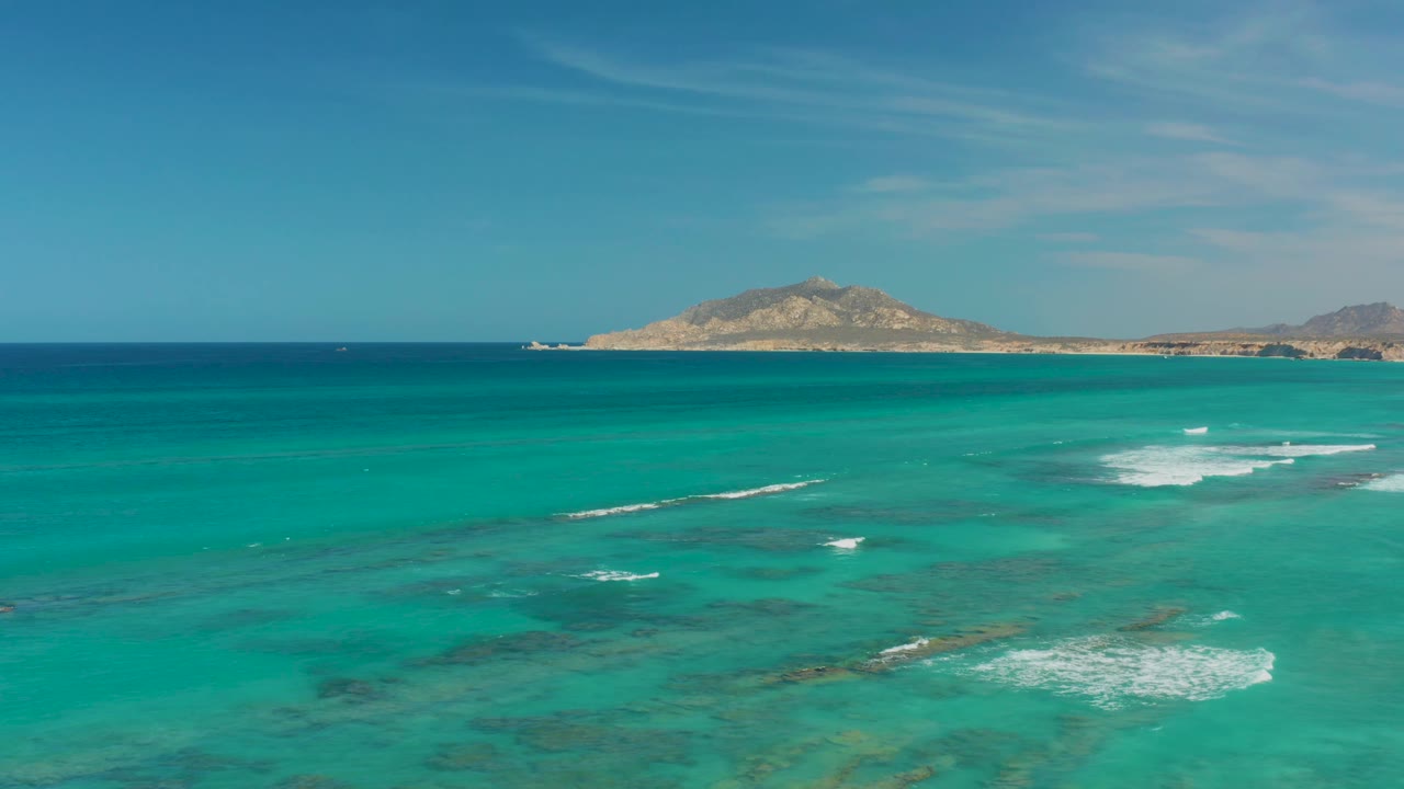 Cabo Pulmo shallows show darker reef or seabed patches beneath turquoise water, with white foam bands in the middle distance and no visible people.