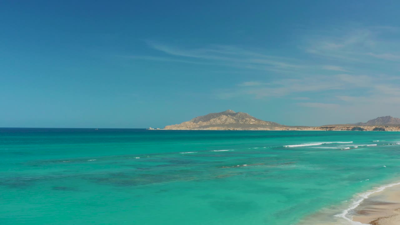 Turquoise ocean, sandy shore, distant landmass, and clear blue sky.
