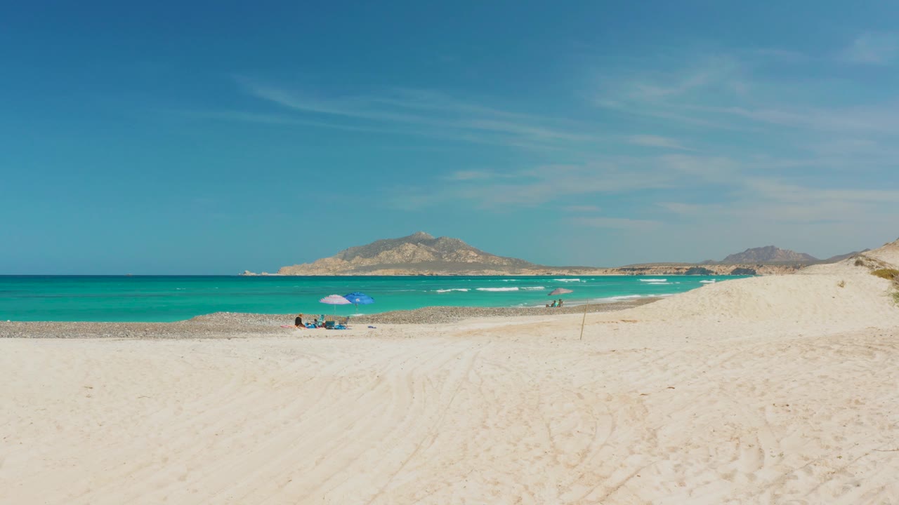Sandy shore and turquoise sea with small beach group under a blue umbrella.