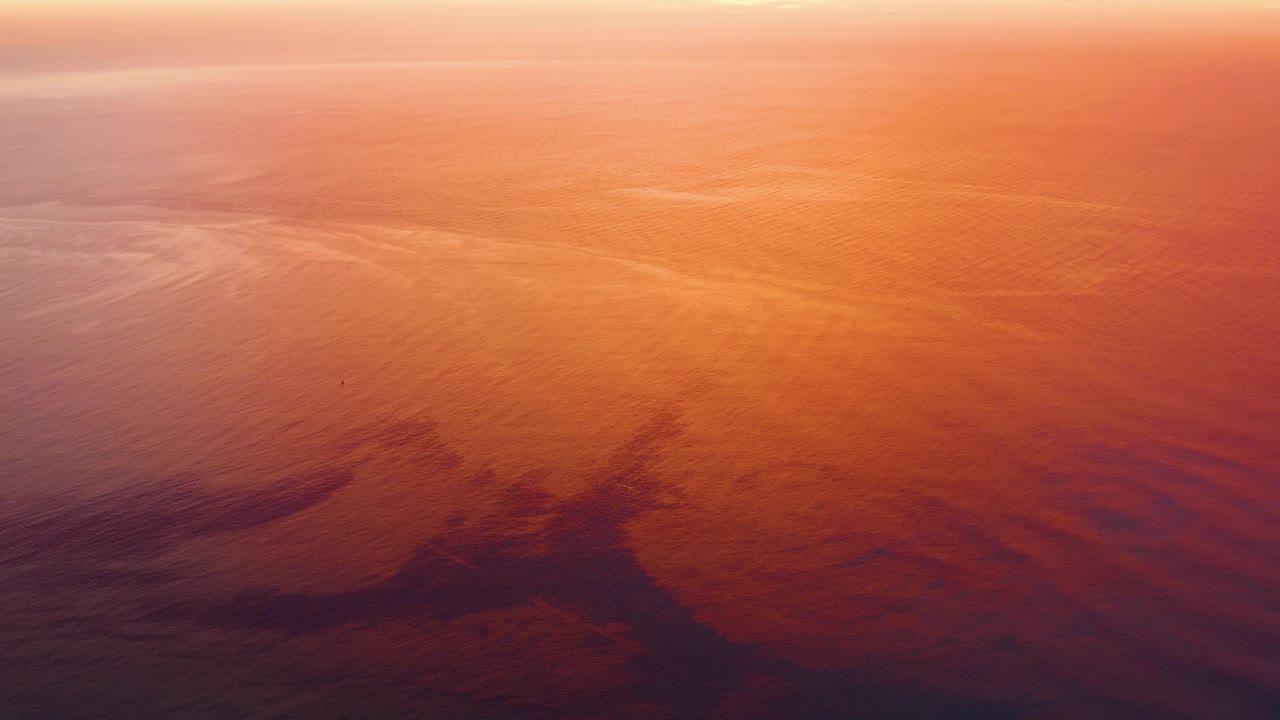 Rippling ocean water in Cabo Pulmo, Baja California Sur, appears orange across the center, with shadowed reflective areas near the lower edge and no visible people.