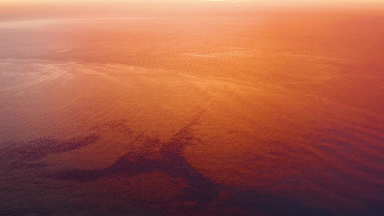 Cabo Pulmo ocean ripples carry warm orange light while the aircraft shadow sits across the lower water, with no visible people.