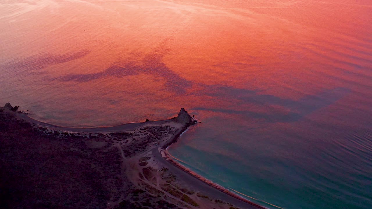 Aerial coastline with pink-orange water and turquoise shallows