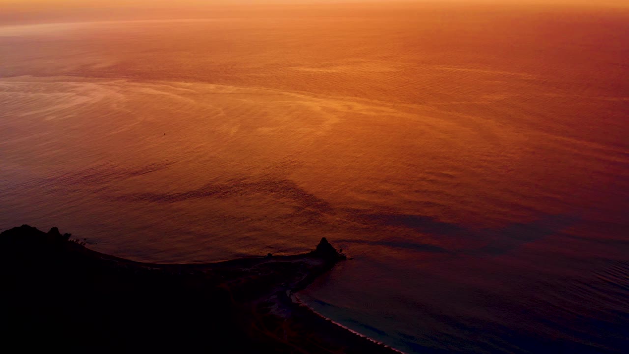 Orange sunset reflected on ocean with dark coastline and pier silhouette