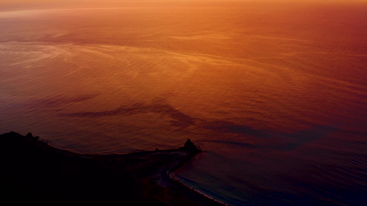 At 0:03, rippled ocean water shows orange and pink bands while the lower Cabo Pulmo coastline stays nearly black, with no visible people in the frame.