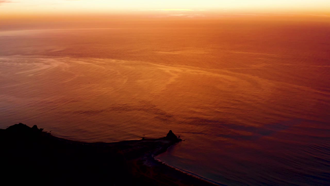 Cabo Pulmo ocean at sunset with pink-orange reflections spread across the water and the coastline held in dark silhouette, no visible people.