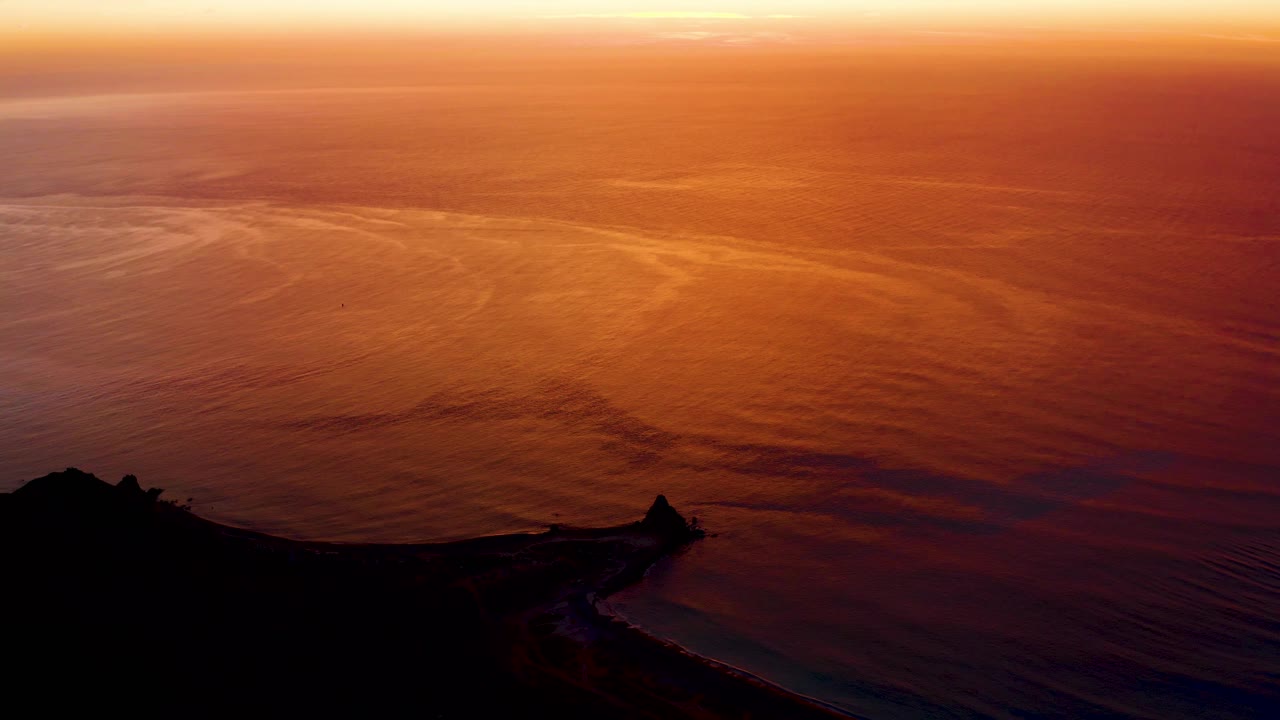 Orange water at sunset with coast in silhouette