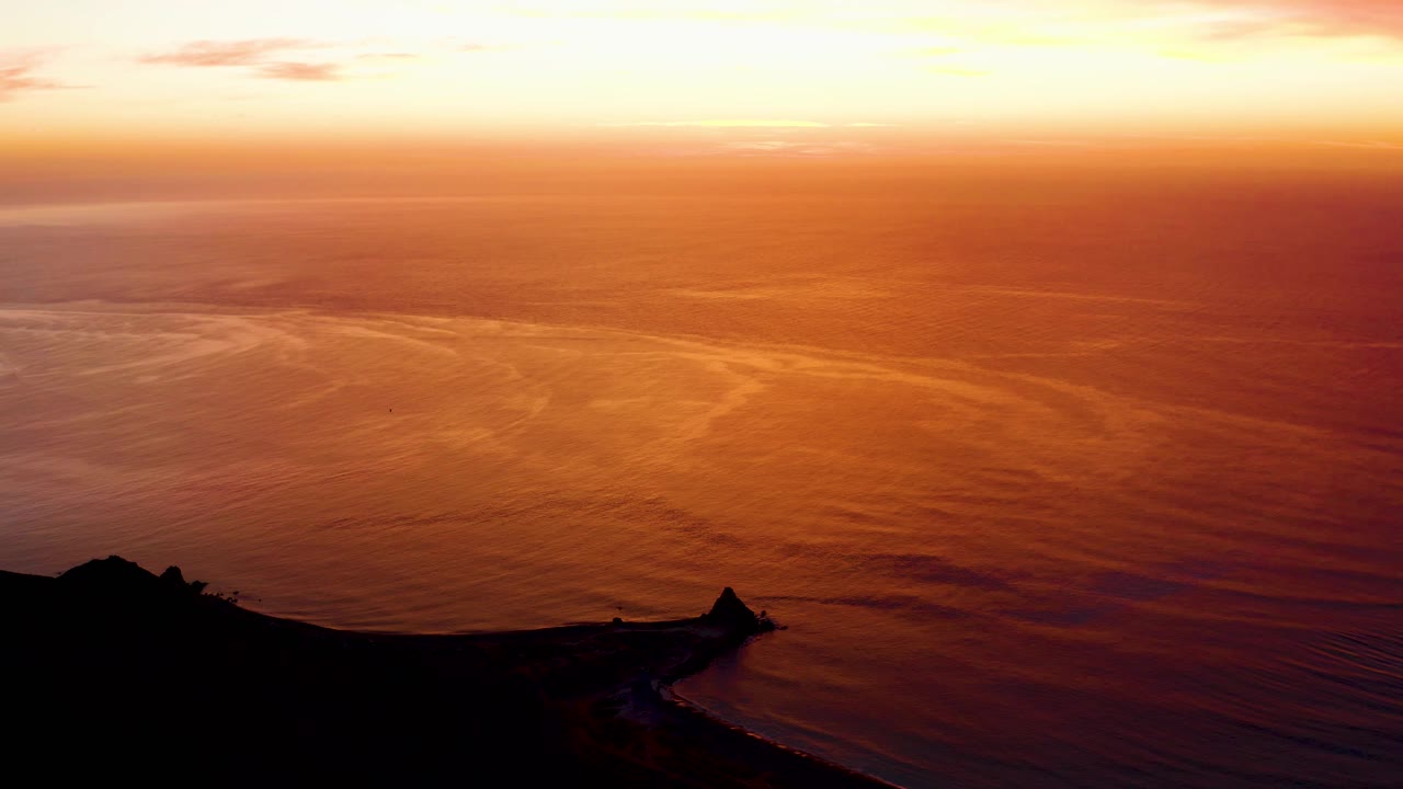 Cabo Pulmo sunset over open water with the cliff silhouette darker at the bottom, fine wave lines across the orange sea, a bright upper sky band, and no visible people.