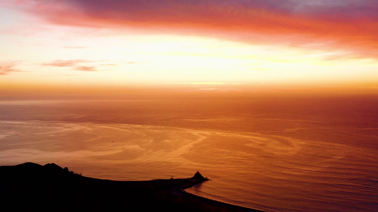Cabo Pulmo sunset view one second in, with the bright horizon stretching across orange water and a black coastal point silhouetted at the bottom, with no visible people.