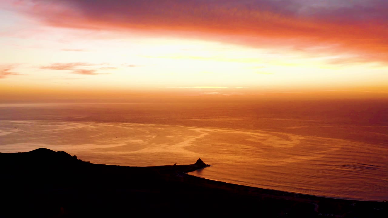 Orange sunset over calm ocean with silhouetted coastline