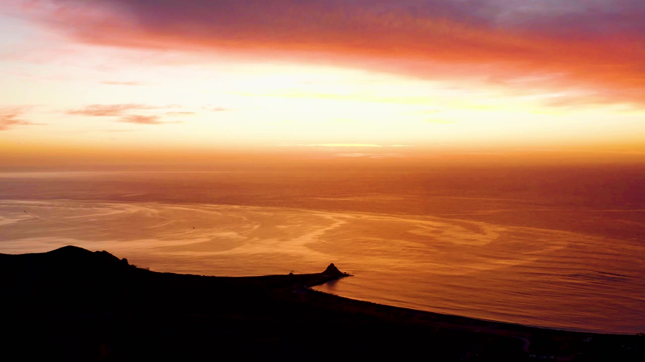 Cabo Pulmo coastal sunset with a bright yellow horizon, orange sea surface, dark foreground land, and no visible people.