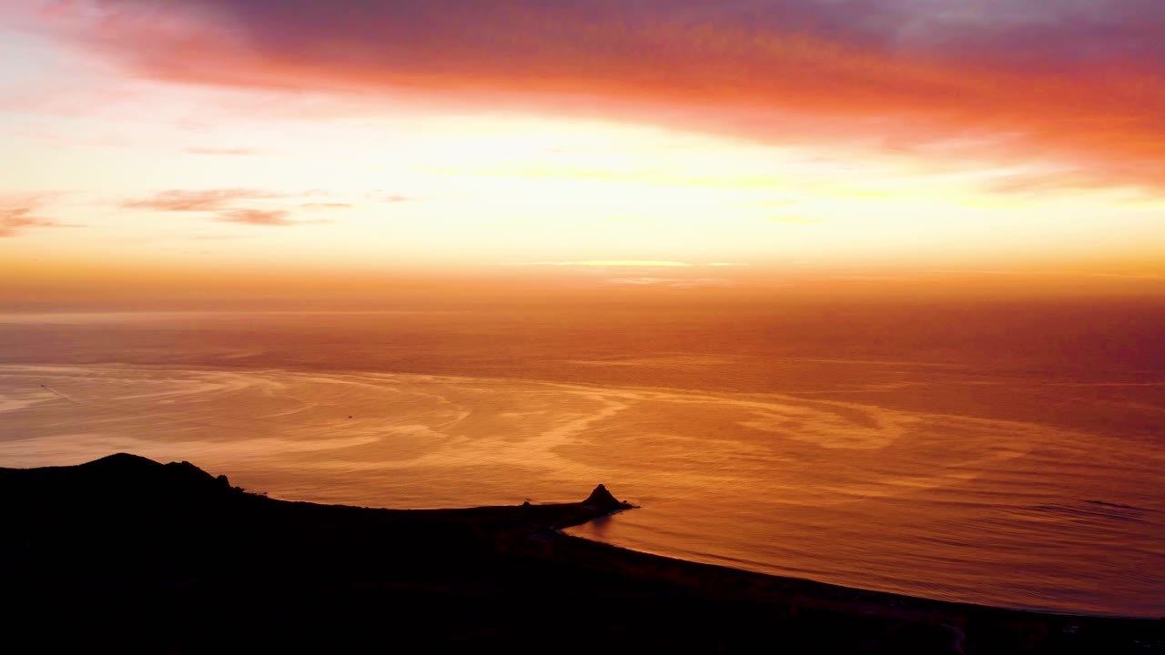 Cabo Pulmo sunset scene where golden reflections stretch over the water below a red-orange cloud band, with no visible people.