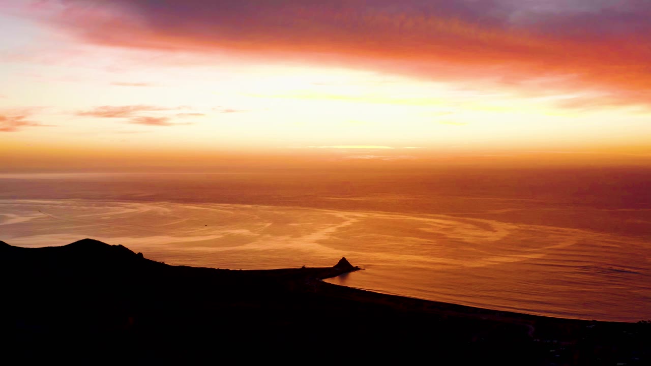 At 0:00, Cabo Pulmo sunset light spreads orange across rippled ocean water behind a black coastal ridge, with no visible people.