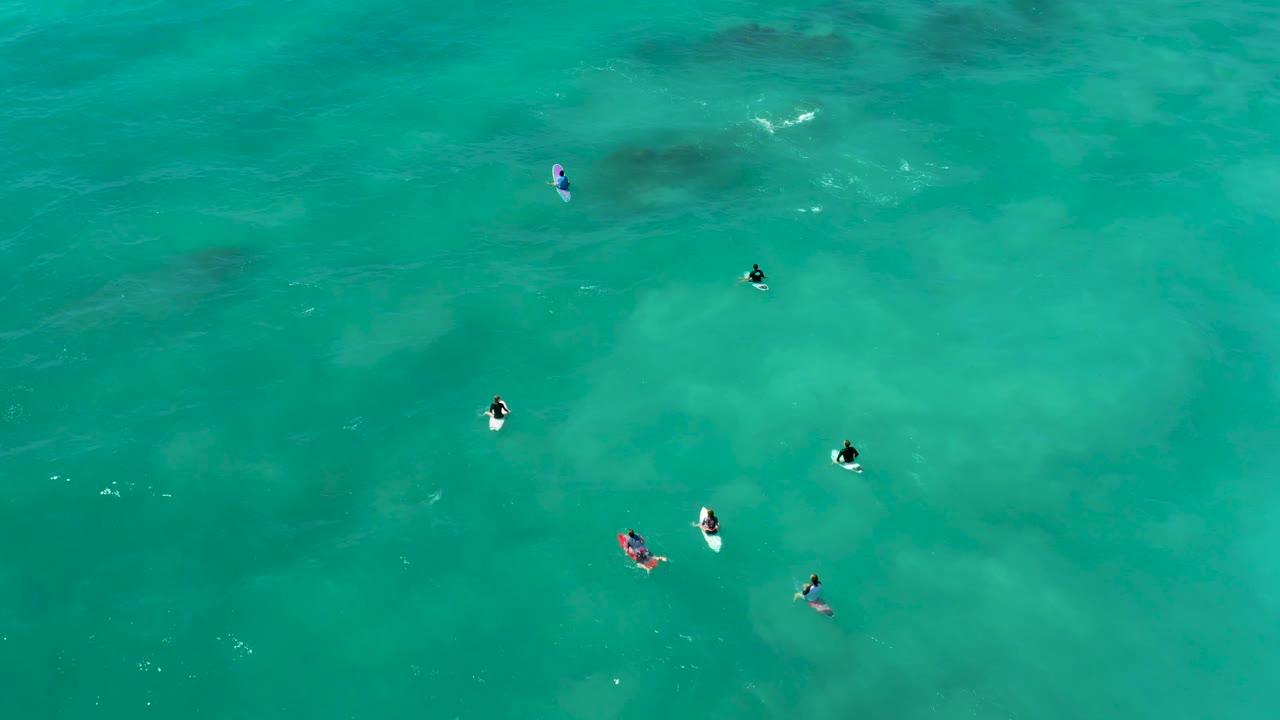 Surfers float on boards in clear blue-green water.