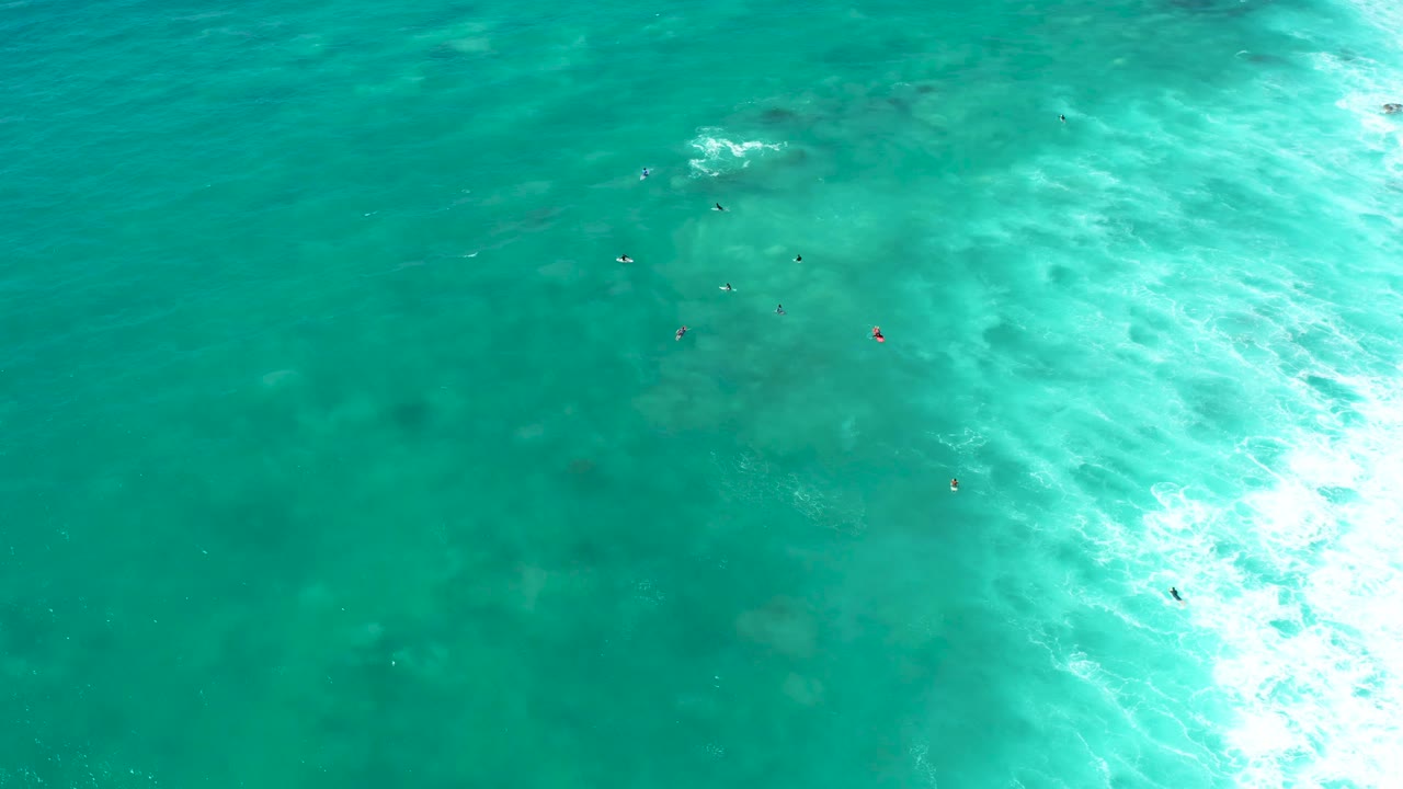 Small swimmers float in clear turquoise water with seabed patches visible beneath.