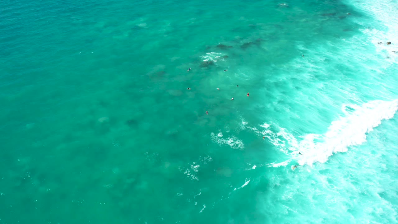 Clear blue-green water with small swimmers and surf foam.